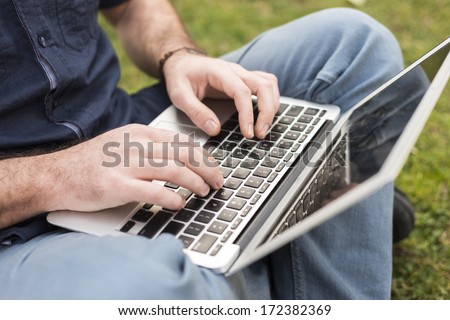 Male hands typing on laptop in the park