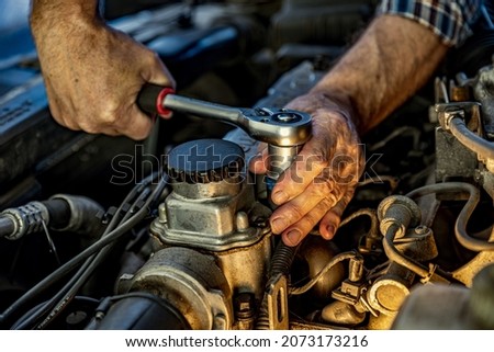 Repairman's male hands with a wrench. Vehicle fitter inspecting used car engine. Car components, belts, hoses, labor arm close up in the open hood of the car. Service center, auto repair shop Foto stock © 
