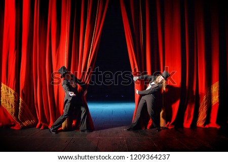 Actor and actress in tuxedos open theater curtain