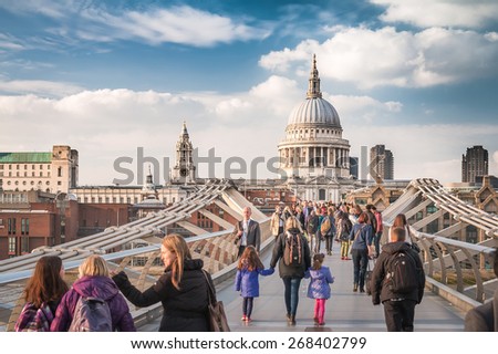 London, UK - April 7, 2015: the Millennium Bridge to the St Paul\'s Cathedral, two famous landmarks of London, with Pedestrians in Blue Sky of Day time