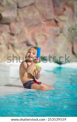 Funny little boy plays with water toy in the swimming pool