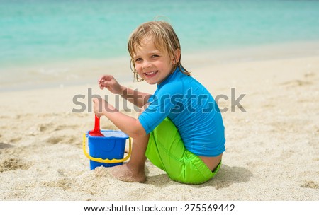Smiling little boy plays in the sand at the beach
