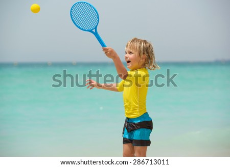 Happy little boy plays beach tennis and has fun on summer vacation
