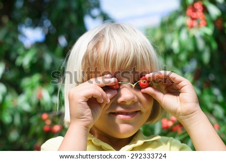 Funny blond  boy covers eyes with cherries in cherry garden