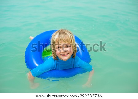 Smiling little boy with blue life ring has fun in the water