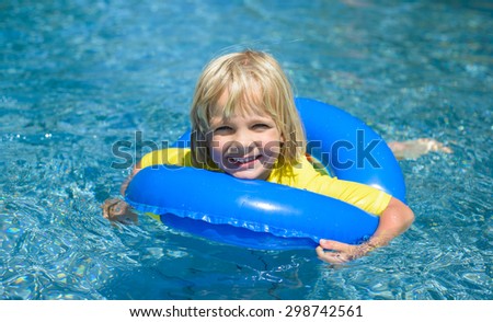 Happy little boy  with blue life ring has fun in the swimming pool