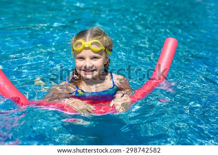 Happy little girl swimming with a pink foam noodle in a pool while on summer vacation