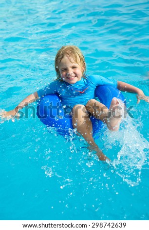 Happy little boy with blue life ring has fun in the swimming pool