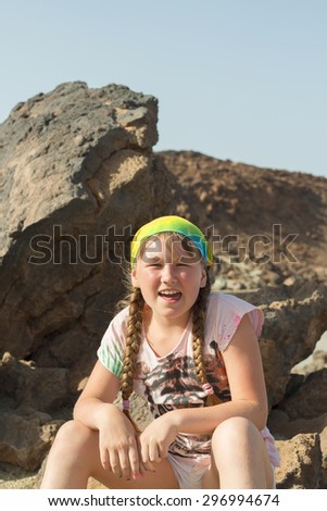 Little girl is sitting and smiling on the stone at the mountains. Kid hiking in the mountains in  Canary Islands.