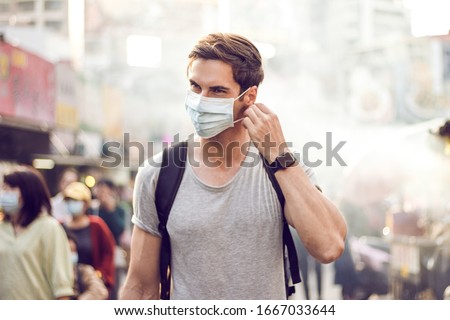Young handsome man walking around night market in Taipei with backpack and wearing a face pollution mask to protect himself from the coronavirus.