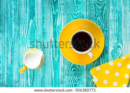 black tea on yellow plate and yellow milk jug
on turquoise colored old wooden table with yellow napkin at polka dots top view