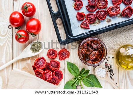tomato fruits,  dried tomatoes on pan, dried  tomatoes in jar, olive oil in sauce-boat, basil, and herbs in wooden spoon  on a wooden table. top view