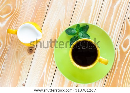 cup of black tea on  light green plate and yellow milk jug\
\
on wooden table with  light green napkin at polka dots. top view