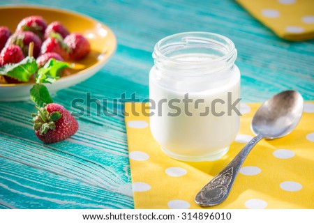 jar of yogurt and strawberry on turquoise colored wooden table, old silver spoon, yellow napkin at polka dots
