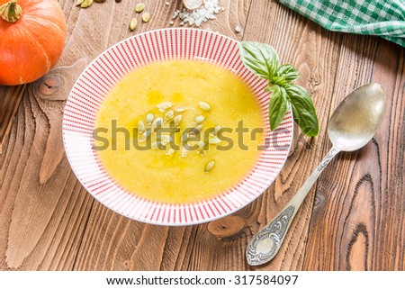 cream soup from pumpkin and other vegetables decorated by basil leaf and pumpkin seeds, basil, pumpkins fruits, salt, pumpkins  seeds  on wooden table with silver spoon and green squared  napkin