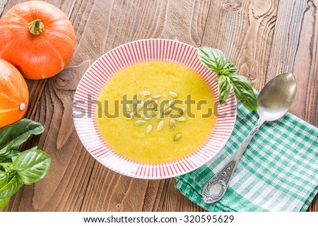 cream soup from pumpkin and other vegetables decorated by basil leaf and pumpkin seeds, basil, pumpkins fruits, salt, pumpkins  seeds  on wooden table with silver spoon on green squared  napkin