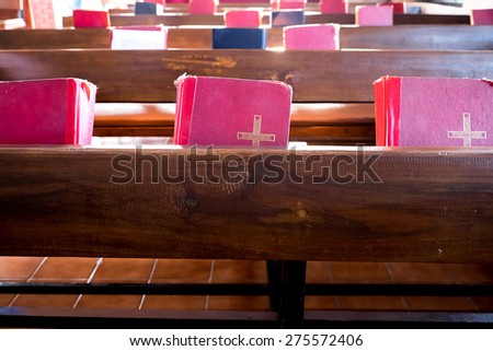 The old red books or red worship songbooks at wooden  bench in church  with soft sun light.
