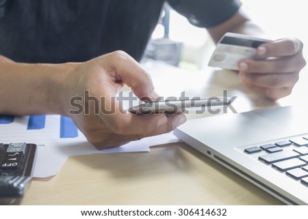 A man holding mobile phone and credit card on laptop for online shopping
