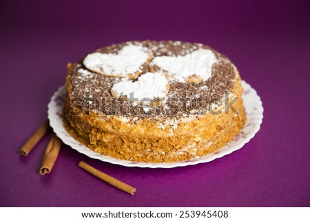 cake with chocolate crumb. Honey cake. Cake hearts. Cake on violet background. Cake with sticks cinnamon. Cinnamon sticks. Cake on white plate. Baked cake. White powder cake. Bake food