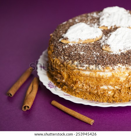 cake with chocolate crumb. Honey cake. Cake hearts. Cake on violet background. Cake with sticks cinnamon. Cinnamon sticks. Cake on white plate. Baked cake. White powder cake. Bake food. Baking