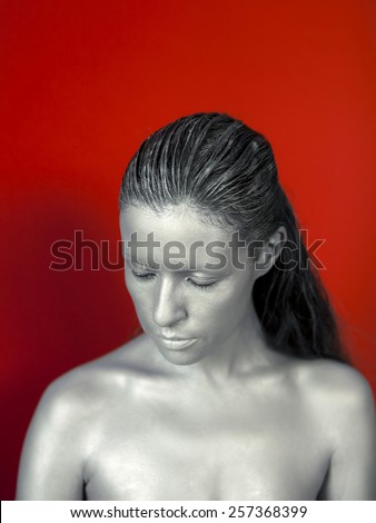 Silver woman face with ring, bijou on red background. Strange kind of woman.