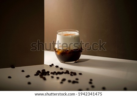 cold espresso coffee with cold milk foam with coffee with brown background  and sprinkled coffee beans on white table