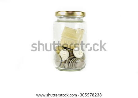 Miniature house inside closed glass jar filled with coins isolated on white background.