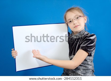 The girl of 9 years in a gray dress shows a hand on a white plastic board where it is possible to place the text.