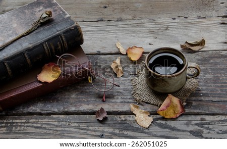 Cup of coffee , petals of an old rose , books , and glasses on a wooden table
