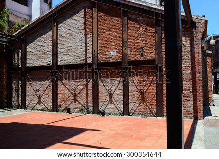 An old brick building supported with steel bars in the sunshine. Shadows on the wall and ground.