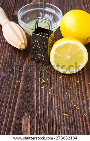 Lemons, lemon juice, lemon zest, wooden citrus squeezer and metal grater on dark wooden board