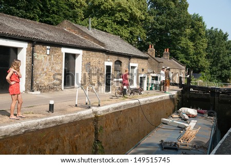 LONDON, ENGLAND - JULY 2013: Narrow boat is ushered through the Old Ford Lock, Regent\'s Canal, London on July 13, 2013. The canals and locks date a century back, are now popular with house-boaters.