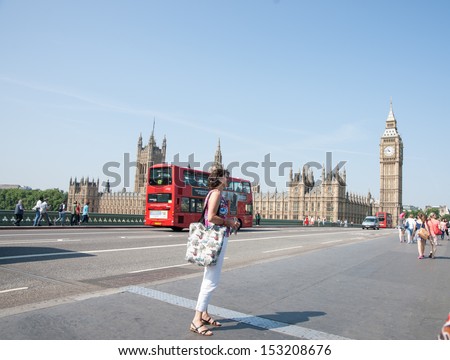 LONDON, ENGLAND - JULY 18: A tourists is photographed on Westminster Bridge with Big Ben and London Double Decker bus in background on July 18,2013. A constant stream of tourists walk over the bridge