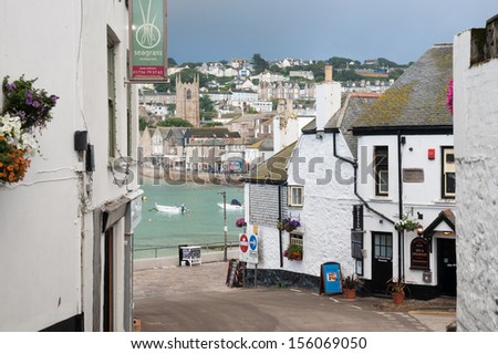 ST. IVES, ENGLAND - JULY 26: Streets lined with buildings in the town with moored boats make a picturesque scene under a dark sky on July 26, 2013. Narrow lanes  in the village lead to the beachfront.