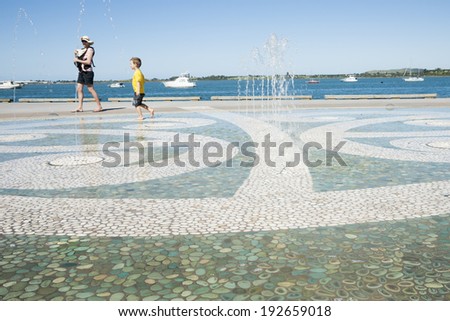 TAURANGA, NEW ZEALAND - JANUARY 28; Mother with baby watches her son playing and enjoying the water feature in Tauranga waterfront playground on January 28, 2014 in Tauranga, New Zealand.