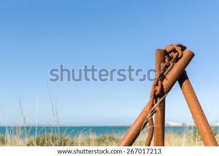 Standing rusty iron pipe and chain with Bluff port in background. The pipe stand has been arranged to lift or hold heavy items and has been left to rust in the yard.