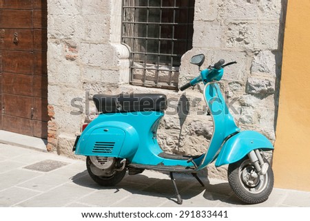 GUBBIO, ITALY -MAY 13; Bright aqua Vespa motor scooter parked in Italian village street under barred window in stone wall.May 13, 2011 in Gubbio, Italy.
