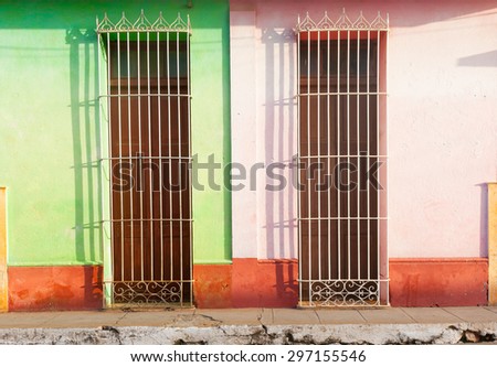 Barred doors two homes differentiated by color and broken pavement in third world town