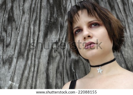 Young girl in front of a weathered piece of plywood looking off in a contemplative manner