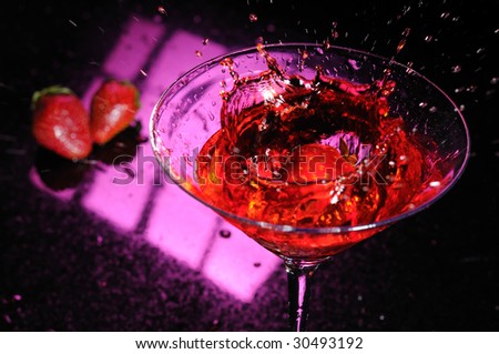 Strawberry splashing down in a martini glass filled with a red liquid