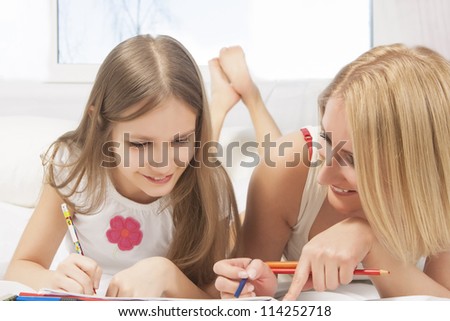 portrait of mother and little daughter together  on bed  drawing pictures using color pencils and smiling