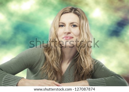 Beauty fashion portrait of young blond woman sitting against artistic background
