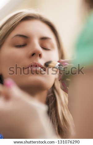 young woman is being applied makeup powder using makeup brush with her eyes closed