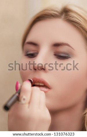 closeup of young blond woman doing makeup with black mascara pencil. shallow depth of field