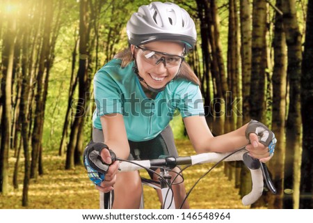 portrait of happy female sportswoman riding a race bike outside in forest, wearing professional biking gear. composite image. horizontal shot.