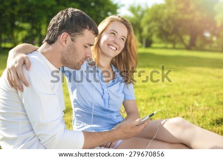 Youth Lifestyle Concept:Happy Relaxing Caucasian Coiple Sitting Together Outdoors. Listening to Music in Headphones. Horizontal Image