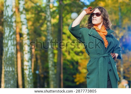 Fashion and Style Concept and Ideas: Good Looking Caucasian Female Model in Green Coat Posing with Sunglasses in Autumn Forest. Horizontal Image Orientation