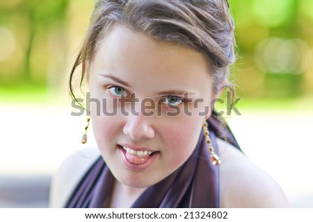 young charming lady with curly fashion hair dressing silk skin standing and making grimace smiling with body turned right and head turned left looking forward in sever violet dress green background