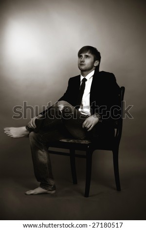 blonde man sitting on old chair turned right looking up,wearing jeans,white shirt,black tie,jacket,with legs crossed appear and hands on free pose isolated