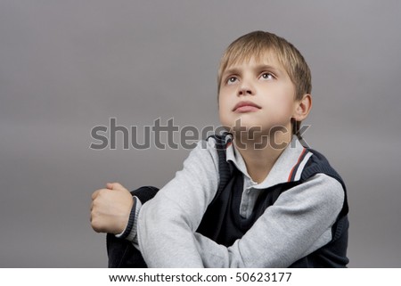 dreaming and relaxing blond caucasian boy with eyes lifted and hands crossed in front isolated over gray background